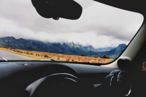 Image is a color photograph of foggy mountains through the windshield of a car; title card for the new short, "Stick Shift," by Jawziya Zaman.